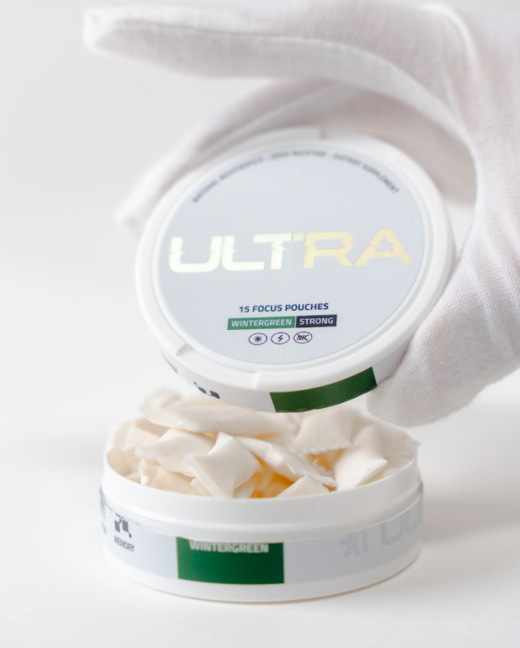 Top-down view of ULTRA pouch tin showcasing open white pouches and lid labeled ULTRA Wintergreen Strong on white background