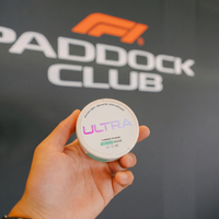 Hand holding Ultra energy pouches tin with holographic ULTRA logo and sweet mint label against blurred Paddock Club backdrop